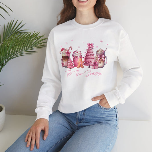 Woman wearing a white sweatshirt with colorful graphics and text, sitting in a room with a plant.