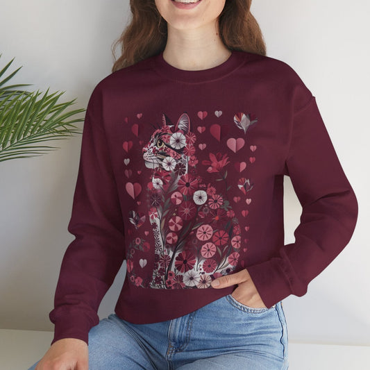 Woman wearing a maroon sweater with floral and cat design sitting on a white surface with a plant in the background.