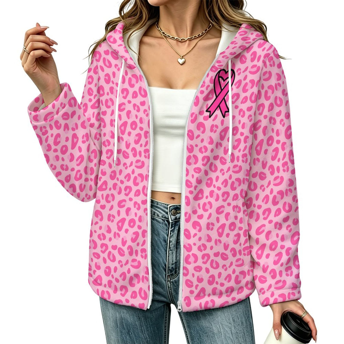 A woman wearing a pink leopard-print zip-up hoodie with a pink ribbon graphic on the chest, styled over a white crop top and blue jeans against a plain white background.
