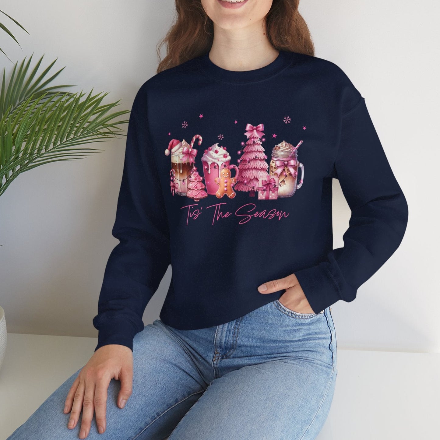Woman wearing a navy blue sweatshirt with colorful graphics and text, sitting on a white surface with a plant in the background.