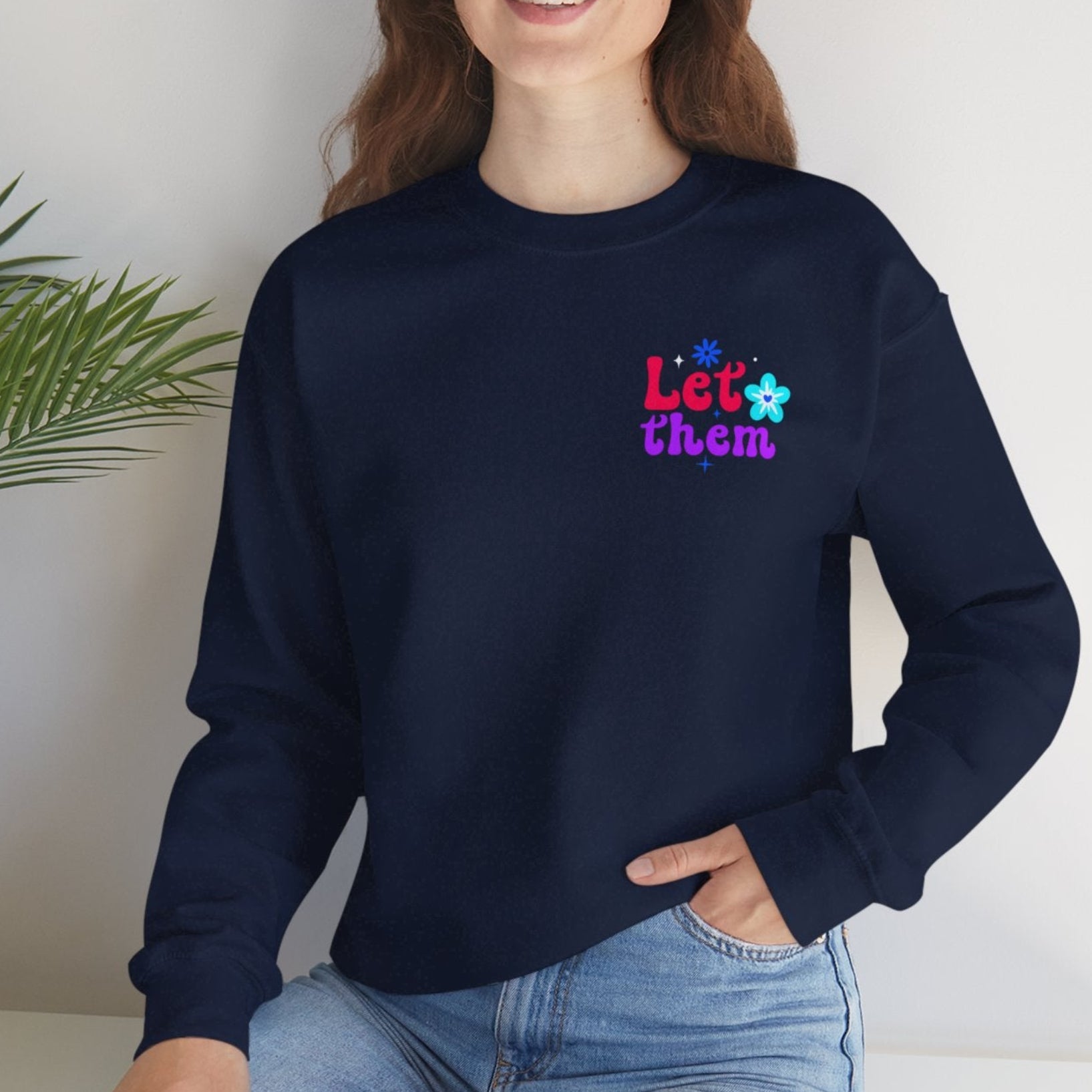 Person wearing a navy blue sweatshirt with colorful text, sitting on a white surface with a plant in the background.