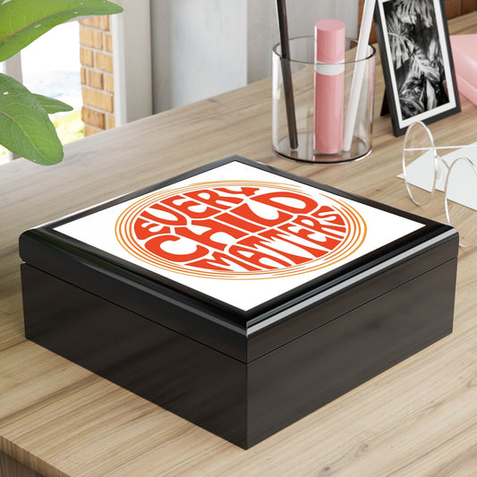 Black box with a white lid featuring an orange design on a wooden surface.