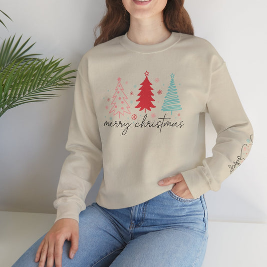 Woman wearing a beige sweatshirt with Christmas tree design and 'Merry Christmas' text, sitting on a white surface with a plant in the background.