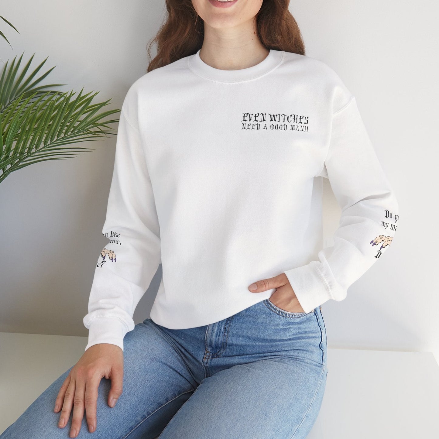 Woman wearing a white sweatshirt with text and graphics, sitting indoors with a plant in the background.
