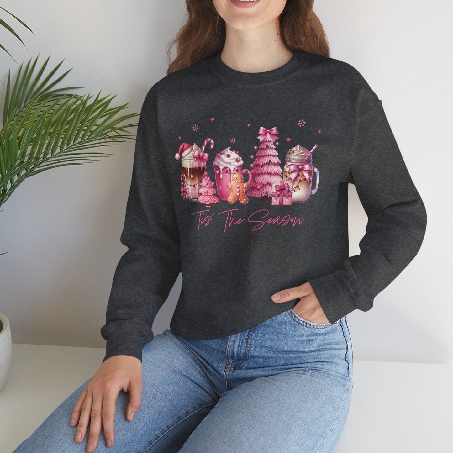 Woman wearing a charcoal sweatshirt with colorful graphics and text, sitting on a white surface with a plant in the background.