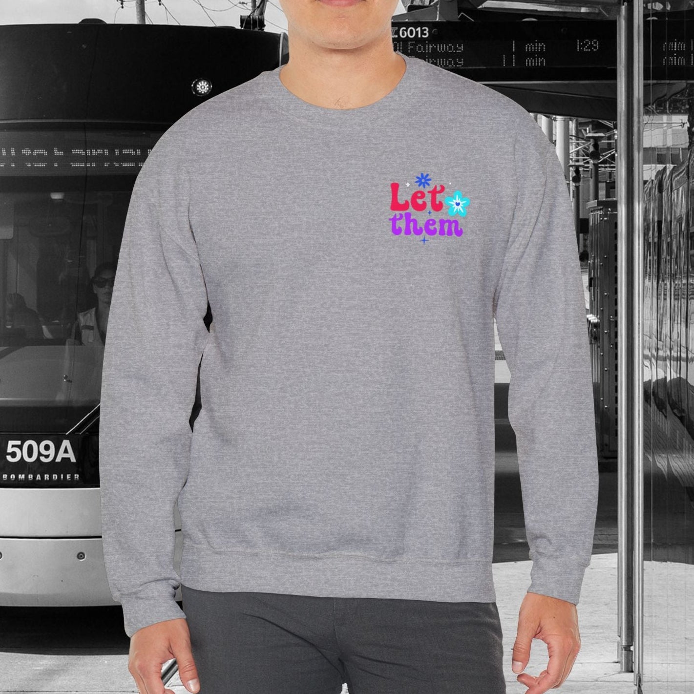 Person wearing a gray sweatshirt with colorful text in an urban setting with a tram.
