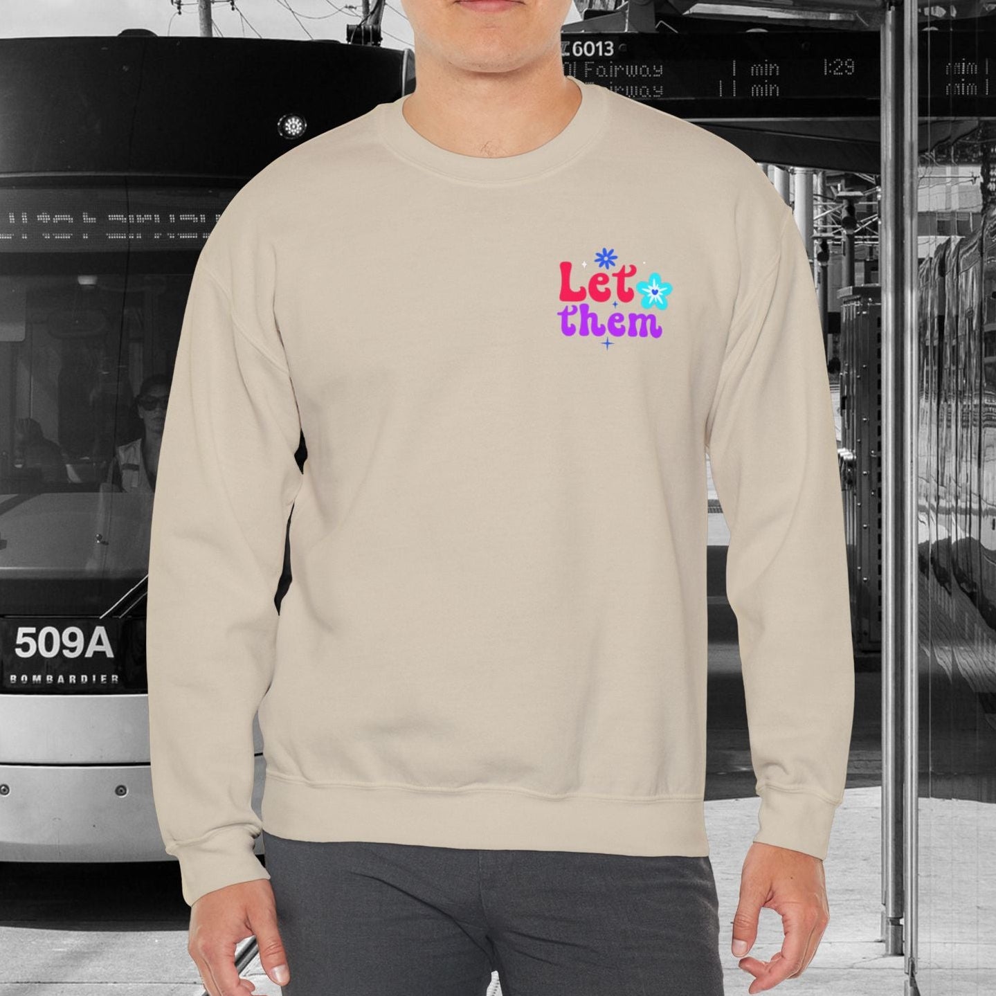 Person wearing a sand sweatshirt with colorful text in an urban setting with a tram.