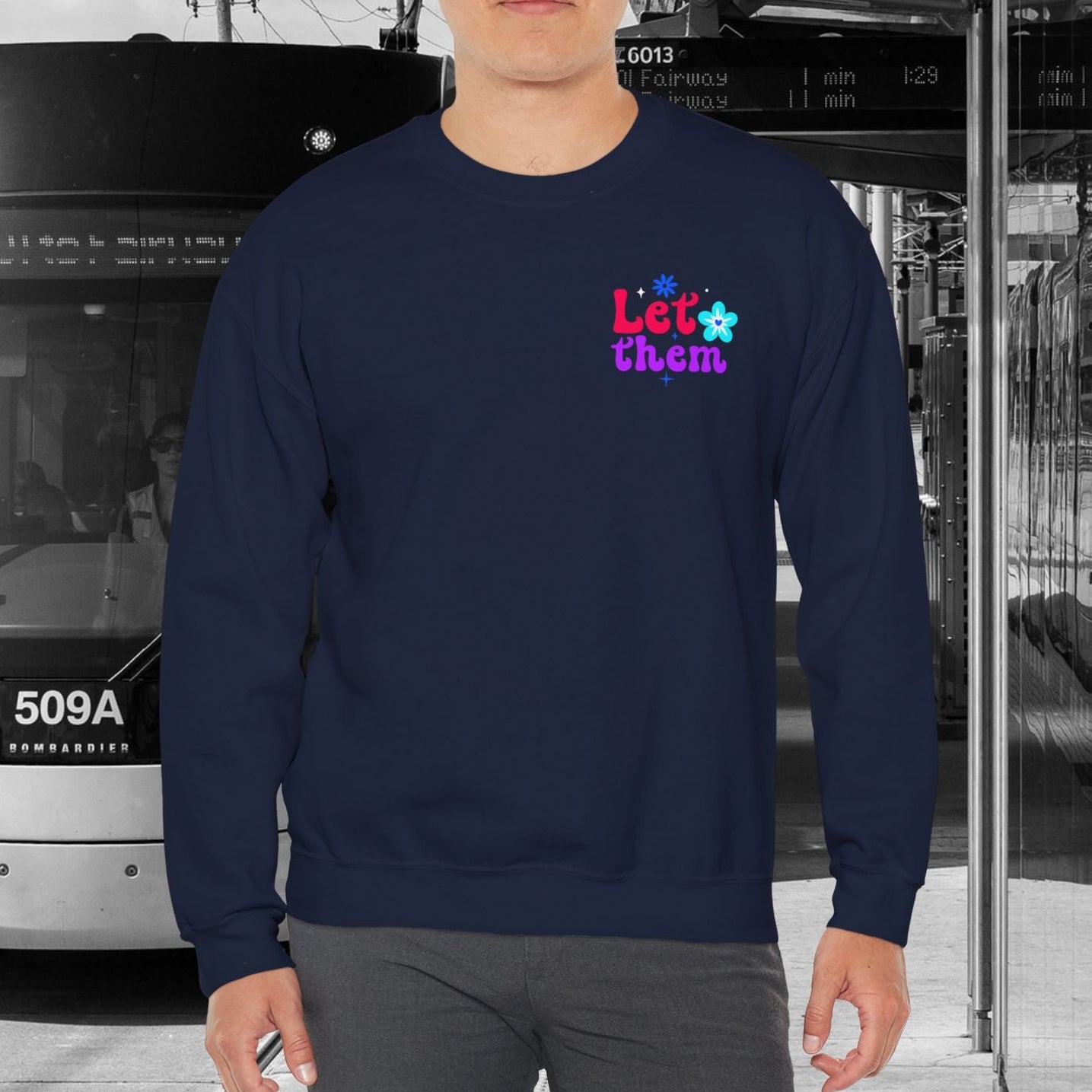 Person wearing a navy blue sweatshirt with colorful text in an urban setting with a tram.