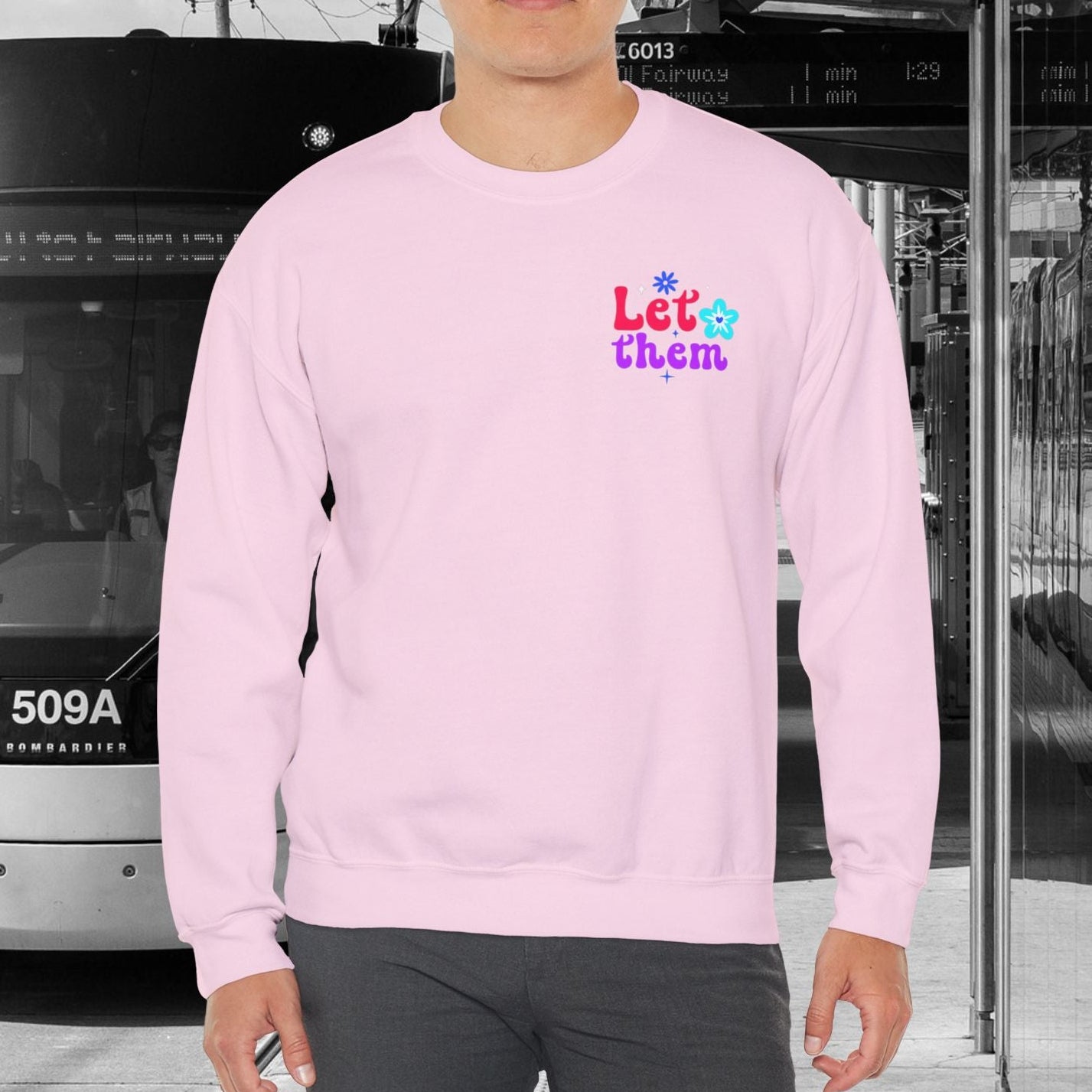 Person wearing a pink sweatshirt with colorful text in an urban setting with a tram.