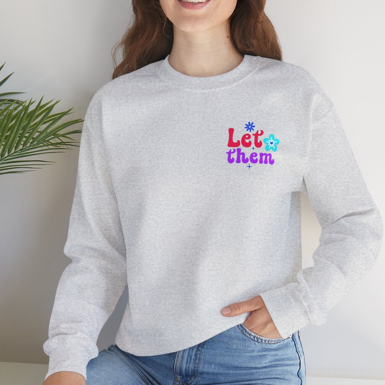 Woman wearing an ash gray sweatshirt with colorful text, sitting in a room with a plant.