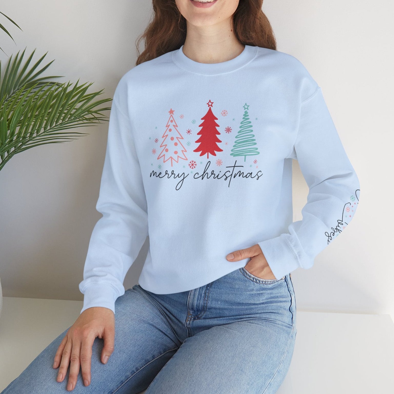 Woman wearing a light blue sweatshirt with Christmas tree design sitting on a white surface.