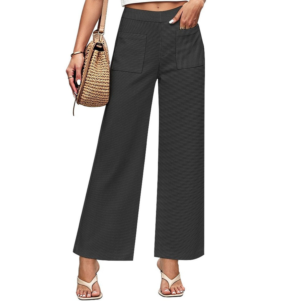 A model wearing dark charcoal gray wide-leg cropped pants with a subtle textured pattern, paired with a white crop top, beige sandals, and a woven straw handbag against a solid white background.