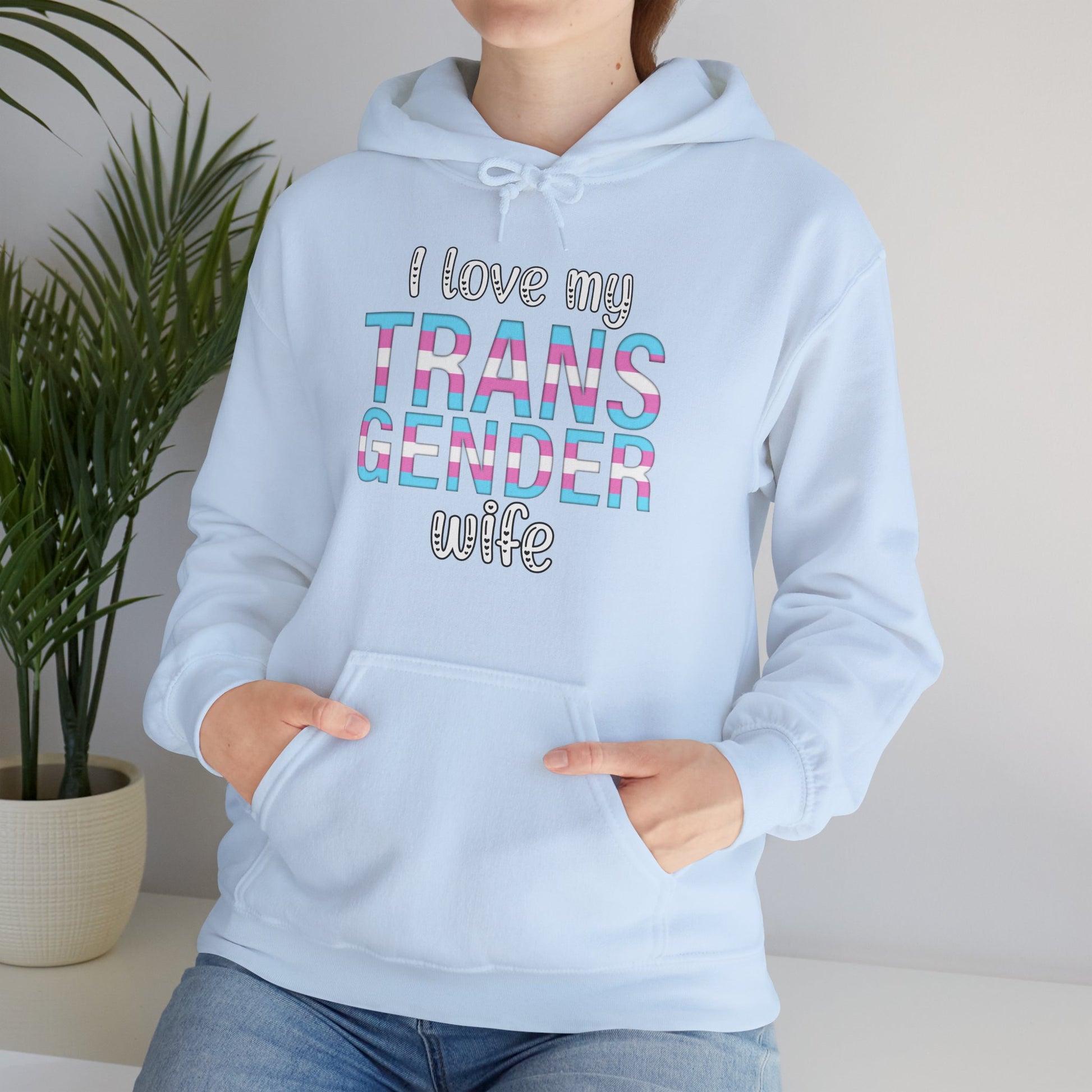 Light blue hoodie with text 'I love my TRANS GENDER wife' worn by a person, with a plant in the background.