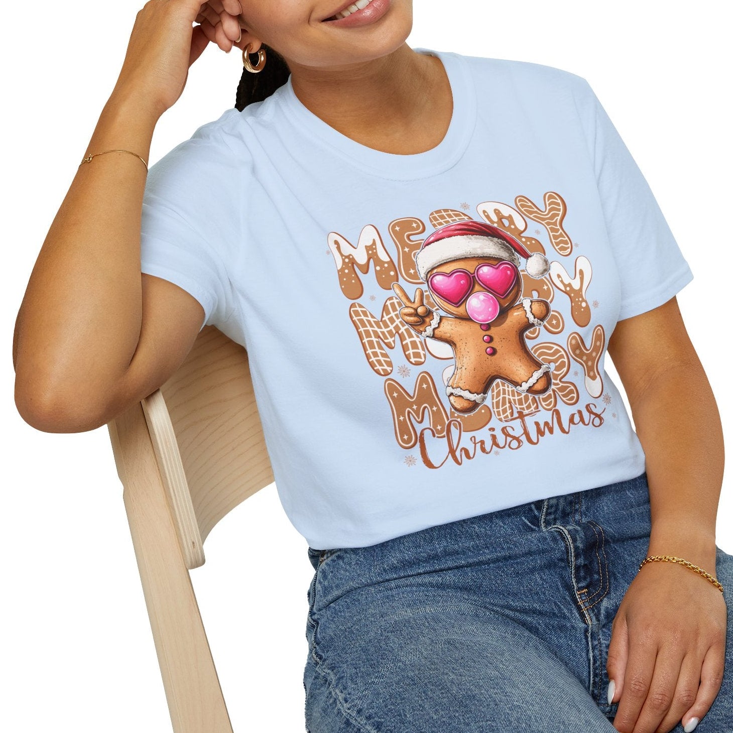 Person wearing a light blue t-shirt with a gingerbread man design and text, sitting on a chair.
