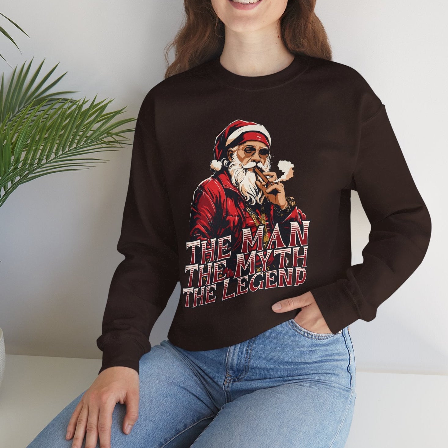 Person wearing a chocolate brown sweatshirt with a graphic design and text, sitting on a white surface with a plant in the background.