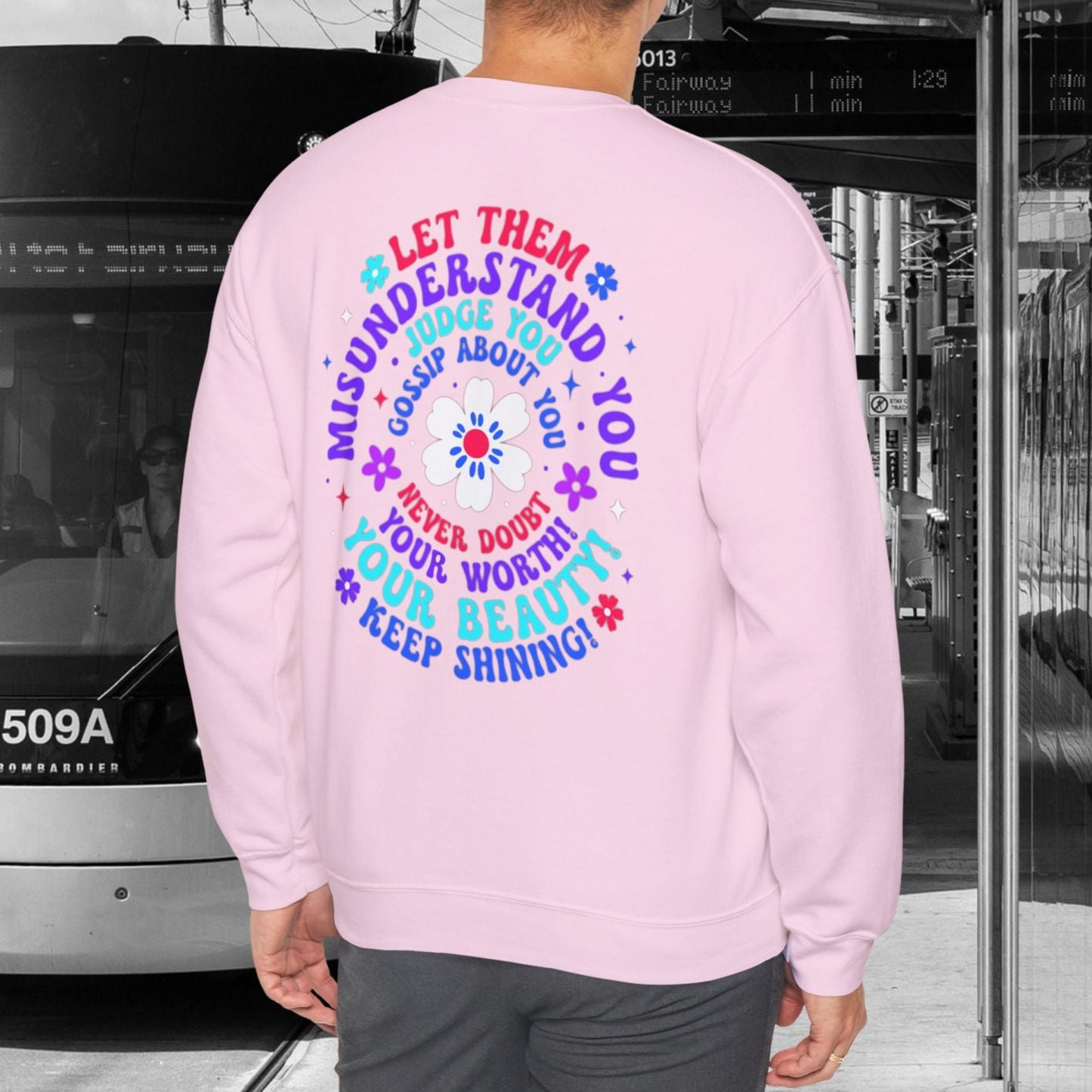 Person wearing a pink sweatshirt with a motivational quote, standing in front of a tram.