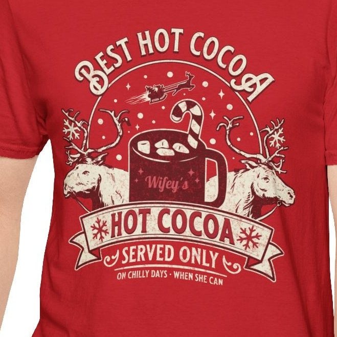 Red t-shirt with a graphic design of hot cocoa, reindeer, and text on a white background