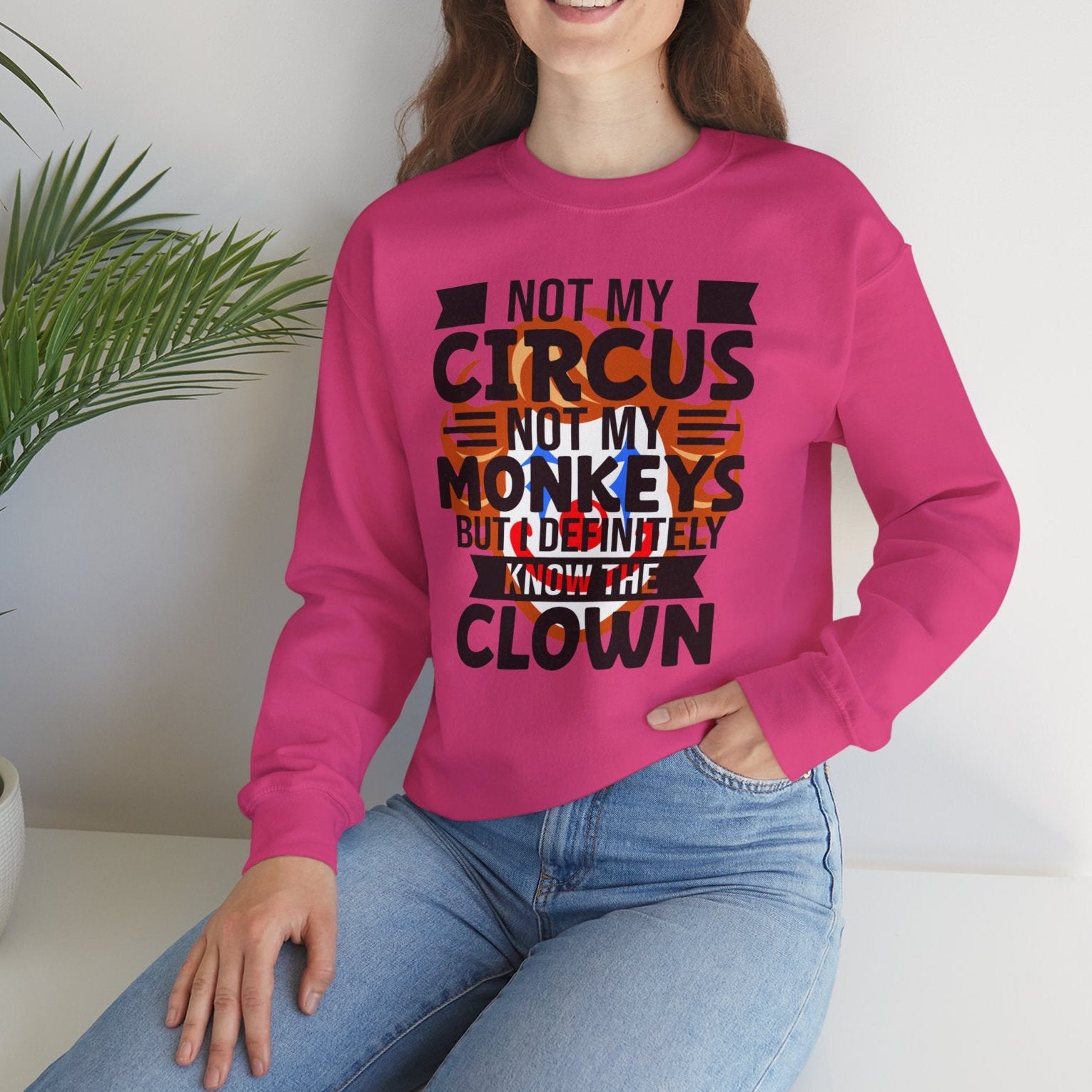 Person wearing a pink sweatshirt with text, sitting on a white surface with a plant in the background.