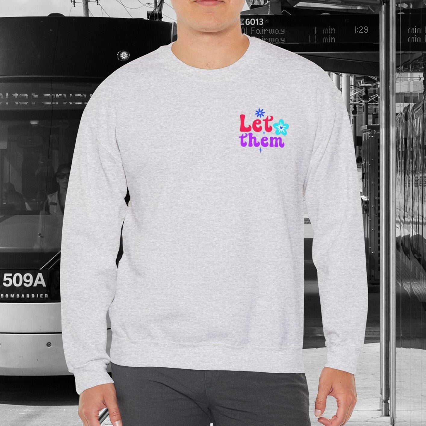 Person wearing an ash gray sweatshirt with colorful text in an urban setting with a tram.
