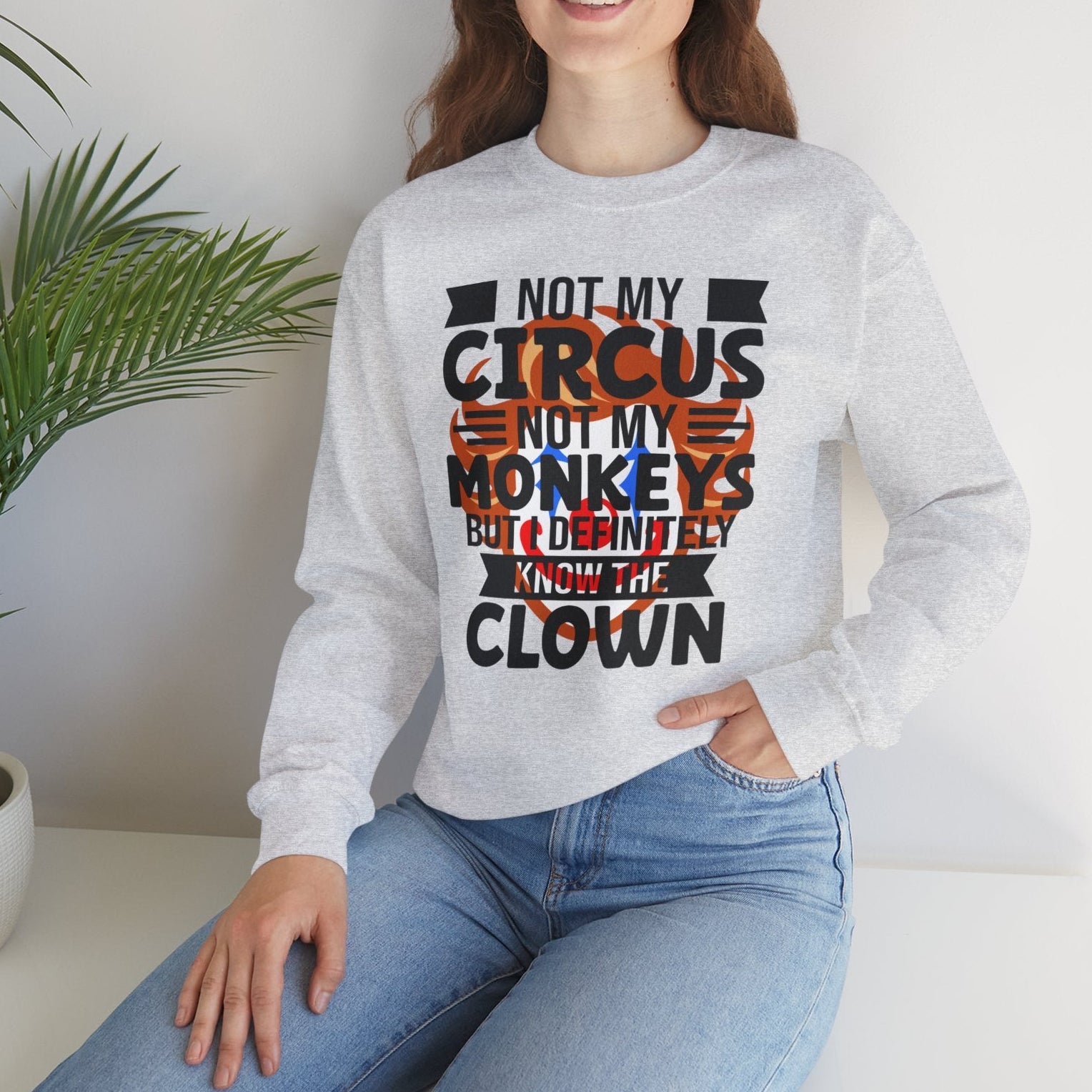 Woman wearing a gray sweatshirt with a humorous quote, sitting in a room with a plant.
