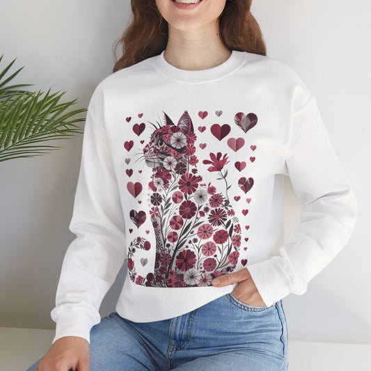 Woman wearing a white sweatshirt with a floral and cat design, sitting in a room with a plant.