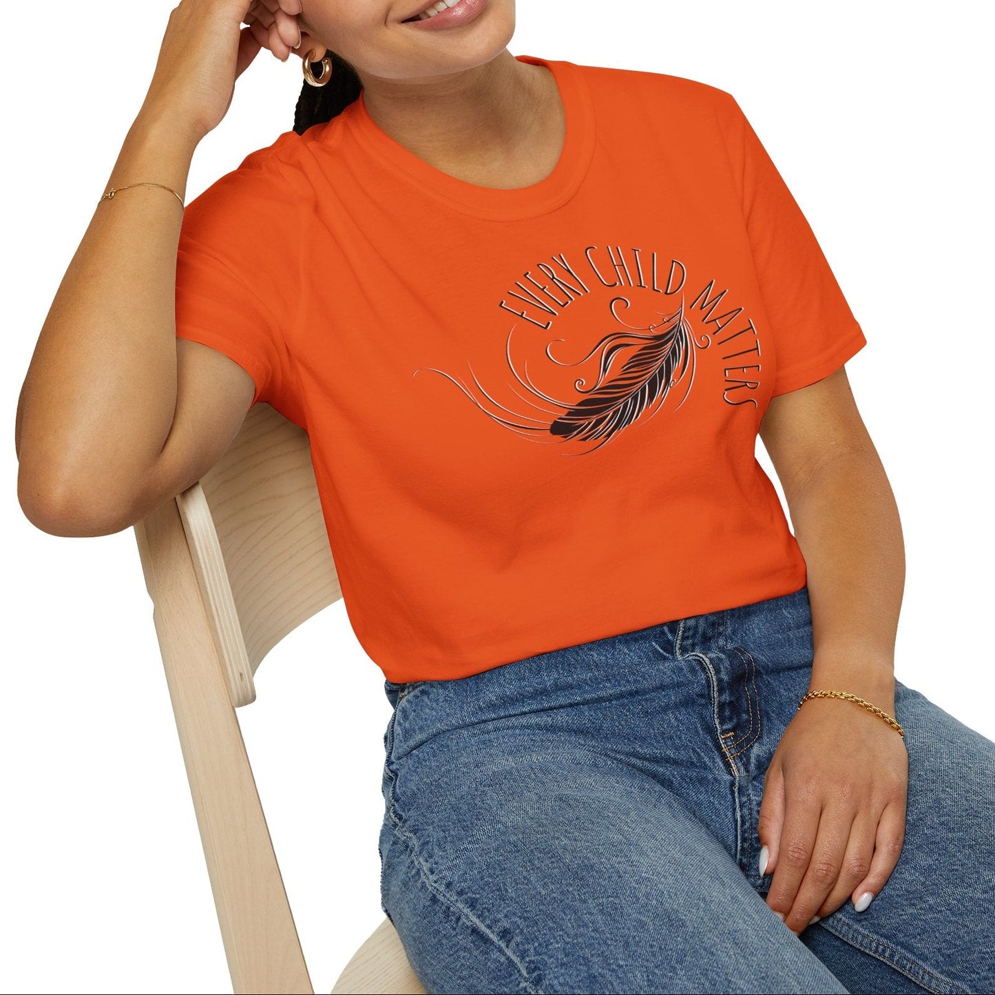 Person wearing an orange t-shirt with a design and text, sitting on a chair against a white background