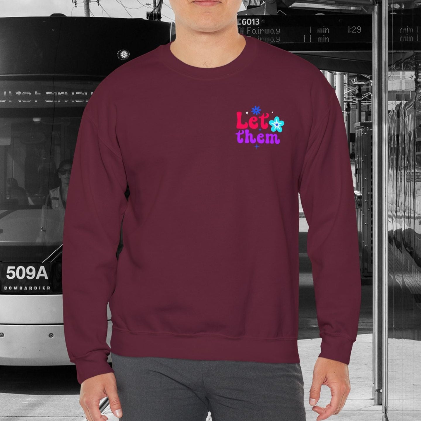 Person wearing a maroon sweatshirt with a logo in front of a tram