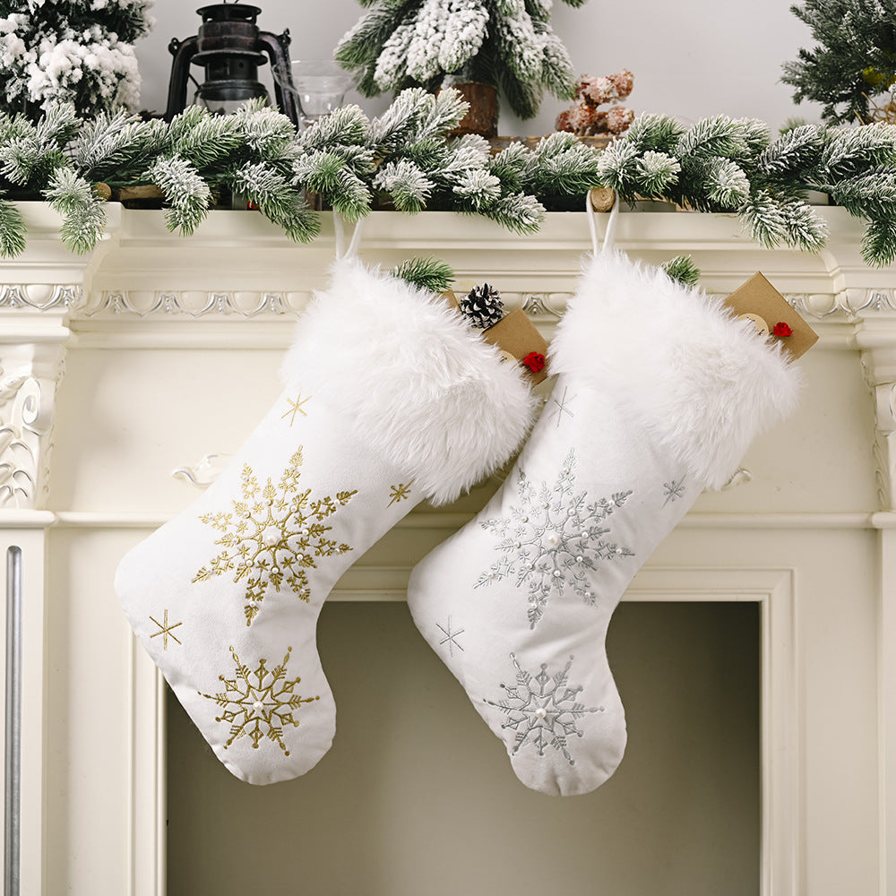 Two white Christmas stockings with snowflake patterns hanging on a fireplace mantle decorated with greenery.