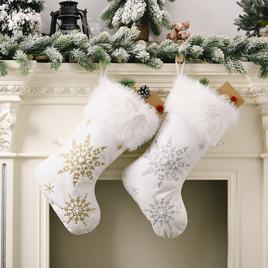 Two white Christmas stockings with snowflake patterns hanging on a fireplace mantle decorated with greenery.