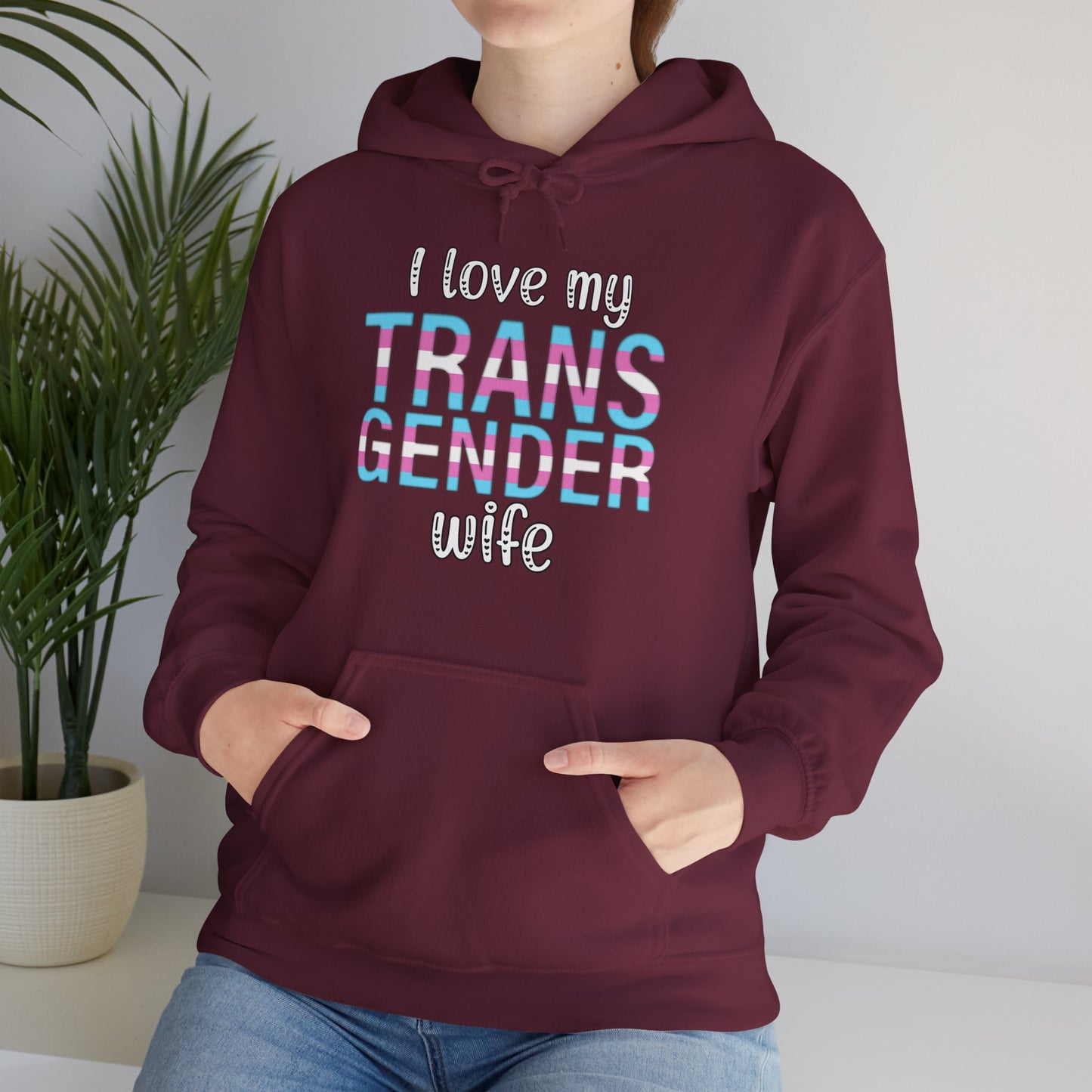 Maroon hoodie with 'I love my TRANS GENDER wife' text, worn by a person indoors.