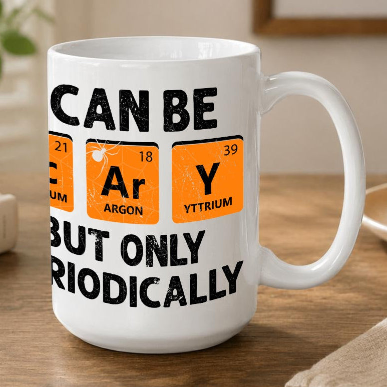 A white ceramic coffee mug with a black and orange periodic table graphic, sitting on a wooden table in a cozy kitchen setting.