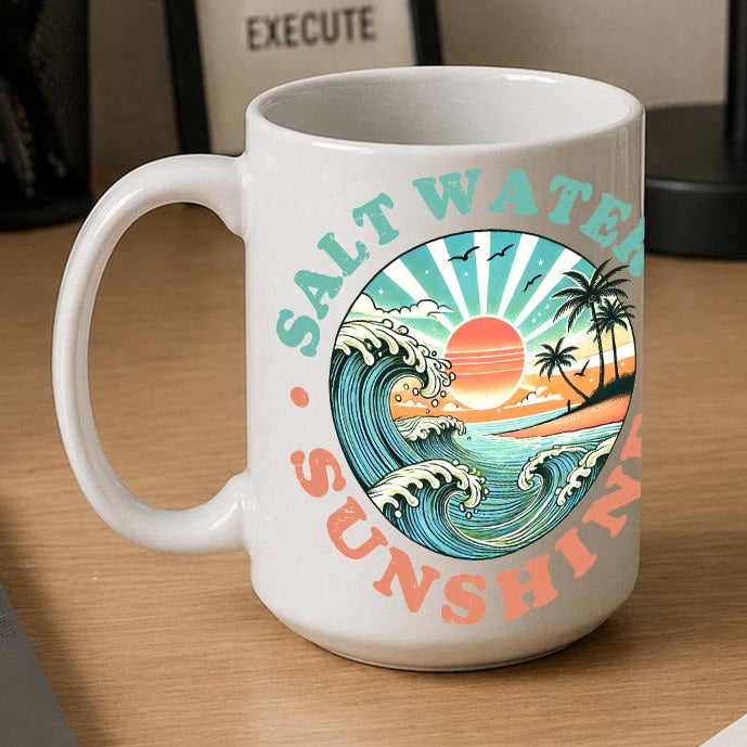 A white ceramic mug with a colourful retro sunset wave graphic and the words 'SALT WATER & SUNSHINE' sits on a wooden desk next to a laptop, notebook, and framed sign.