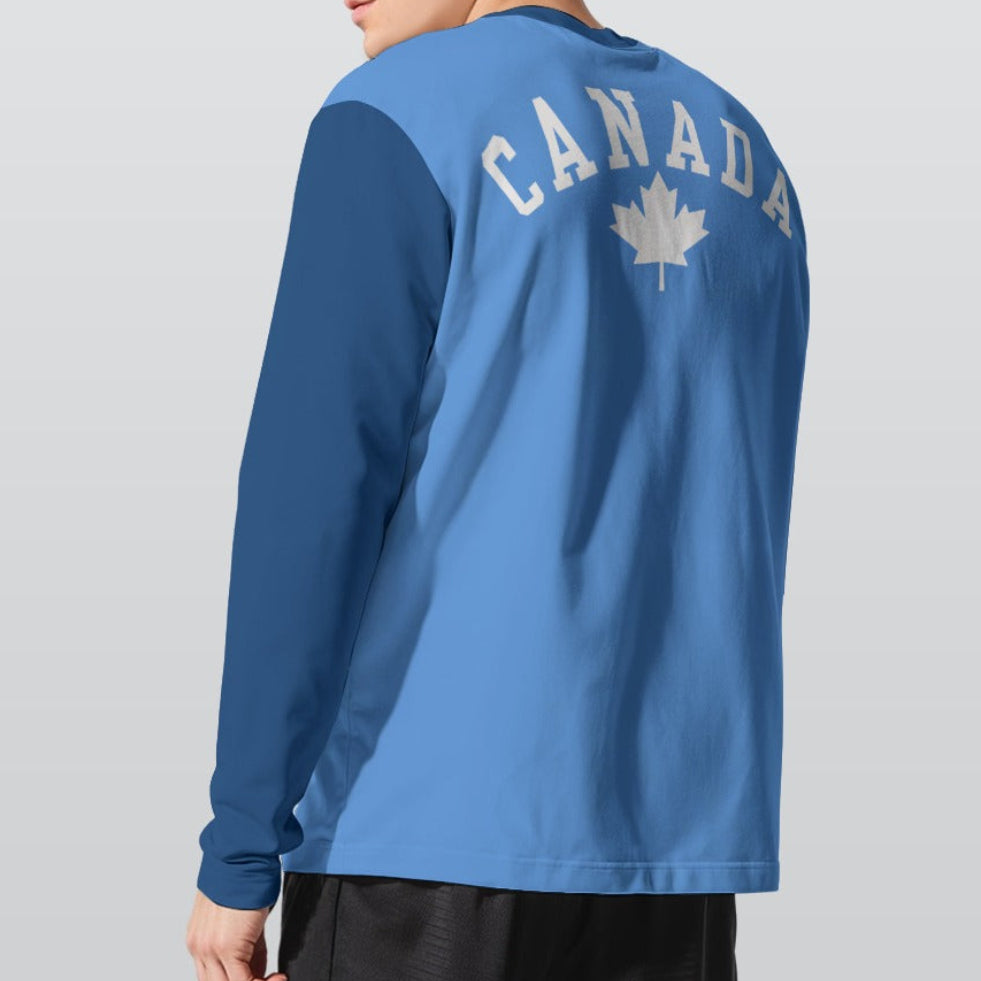 A man wearing a 2-toned blue long-sleeve athletic shirt with 'CANADA' and a maple leaf printed in white on the back, shown from a three-quarters view against a light gray studio background.