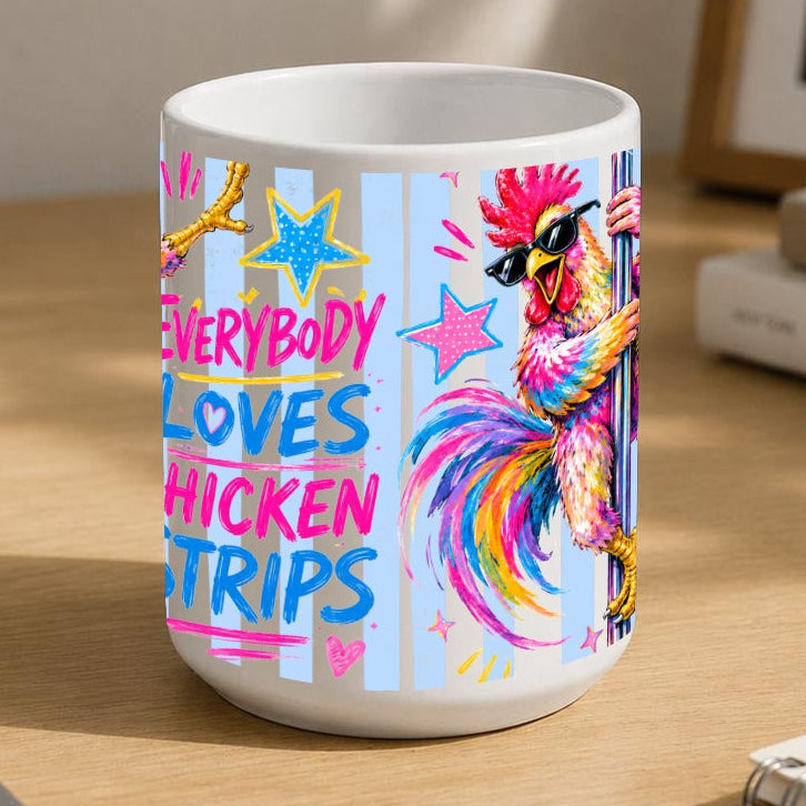 A white ceramic mug with a colourful graphic print of a chicken and the text 'EVERYBODY LOVES CHICKEN STRIPS' sits on a wooden desk in a styled home office setting.