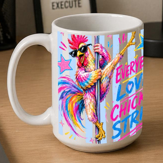 A white ceramic coffee mug with a colourful graphic of a chicken pole dancer and the text 'EVERYBODY LOVES CHICKEN STRIPS' is shown on a wooden desk next to a laptop, notebook, and framed sign.
