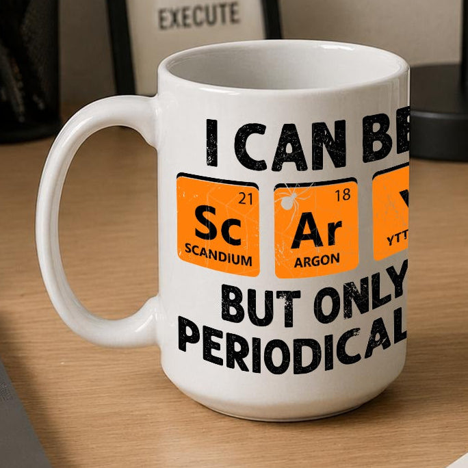 A white ceramic coffee mug with a humorous periodic table graphic sits on a wooden desk next to a laptop, notebook, and framed sign.