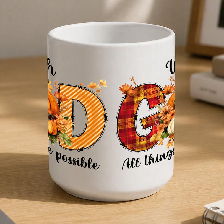 A white ceramic coffee mug with a 'GOD' design featuring autumn-themed letters, placed on a wooden desk next to a laptop, notebook, and plant.