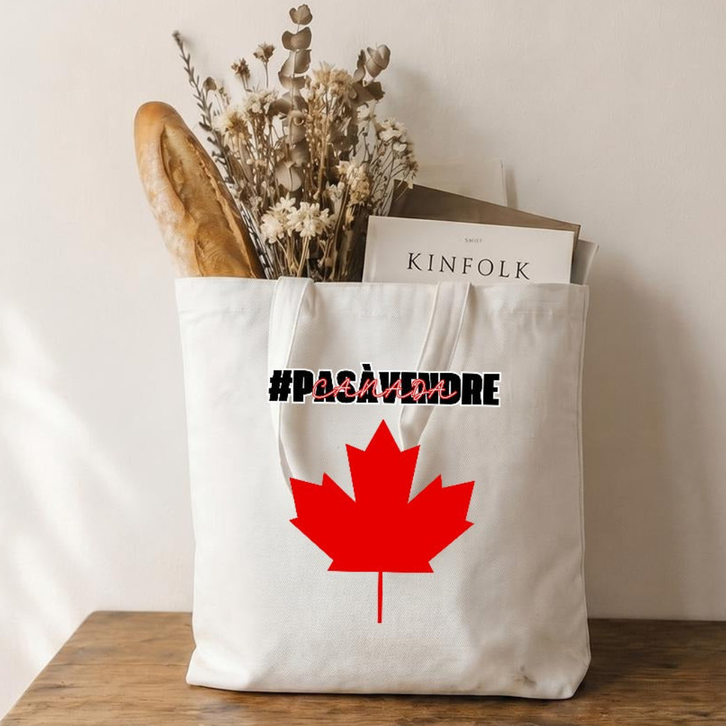 Tote bag with a red maple leaf and text on a wooden table against a beige wall