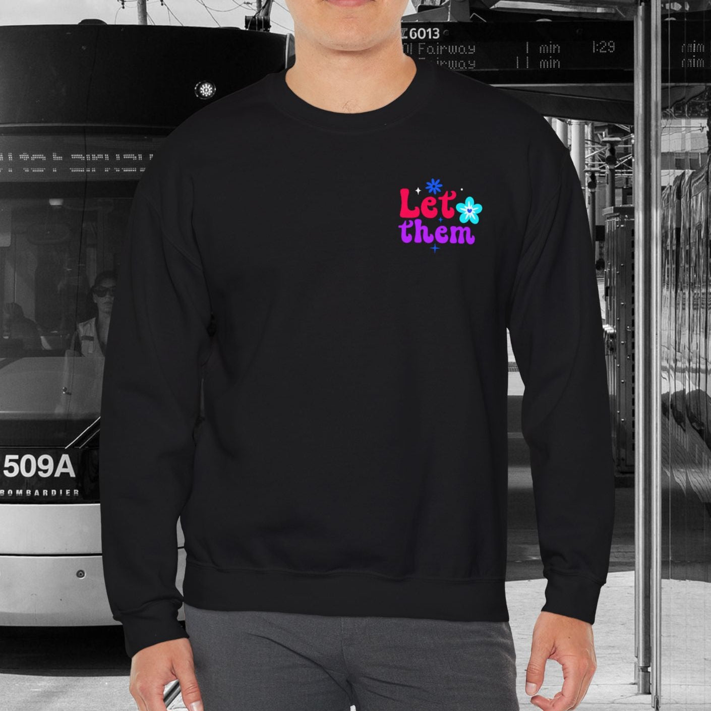 Person wearing a black sweatshirt with colorful text and graphics, standing in front of a tram.