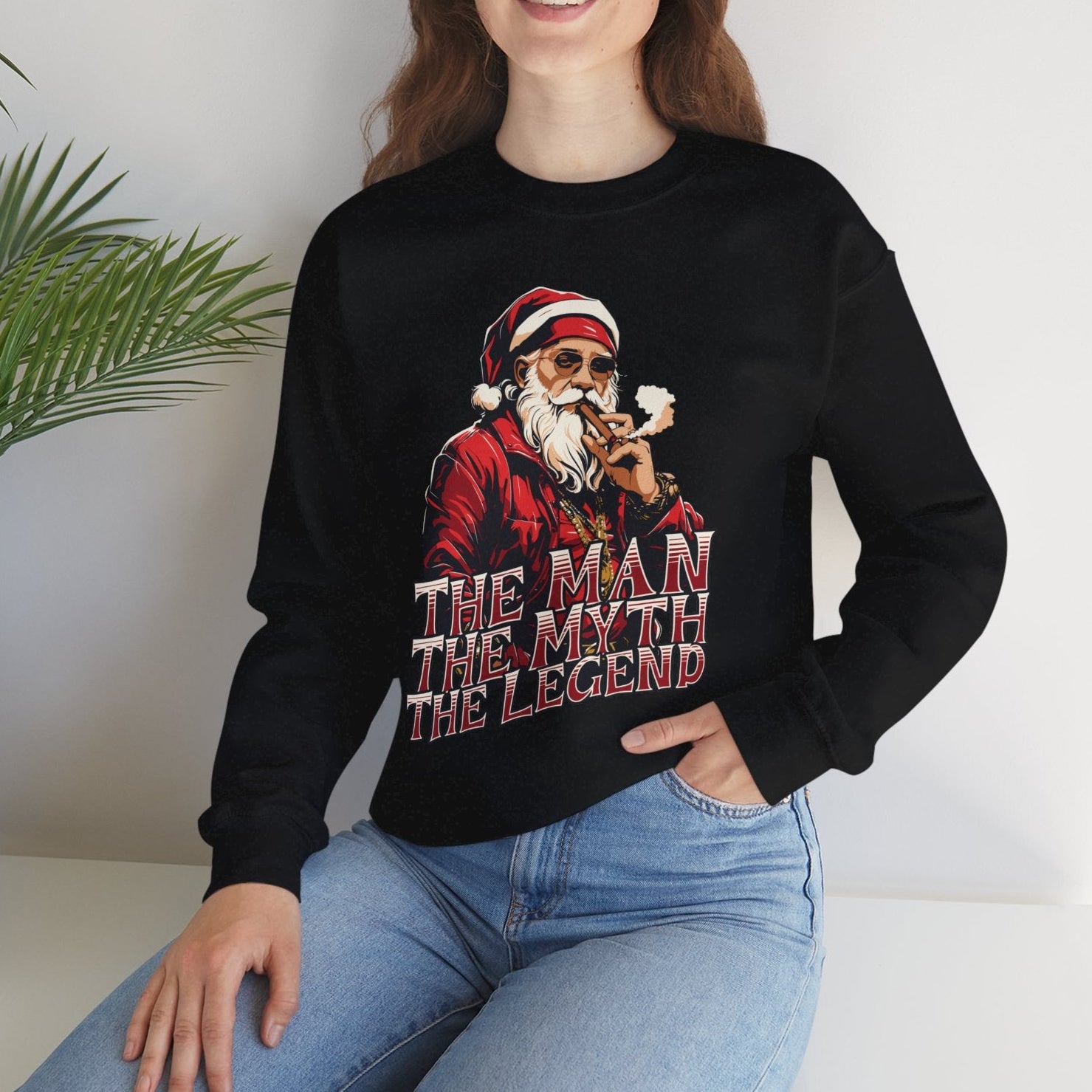 Person wearing a black sweatshirt with a graphic design and text, sitting in a room with a plant.