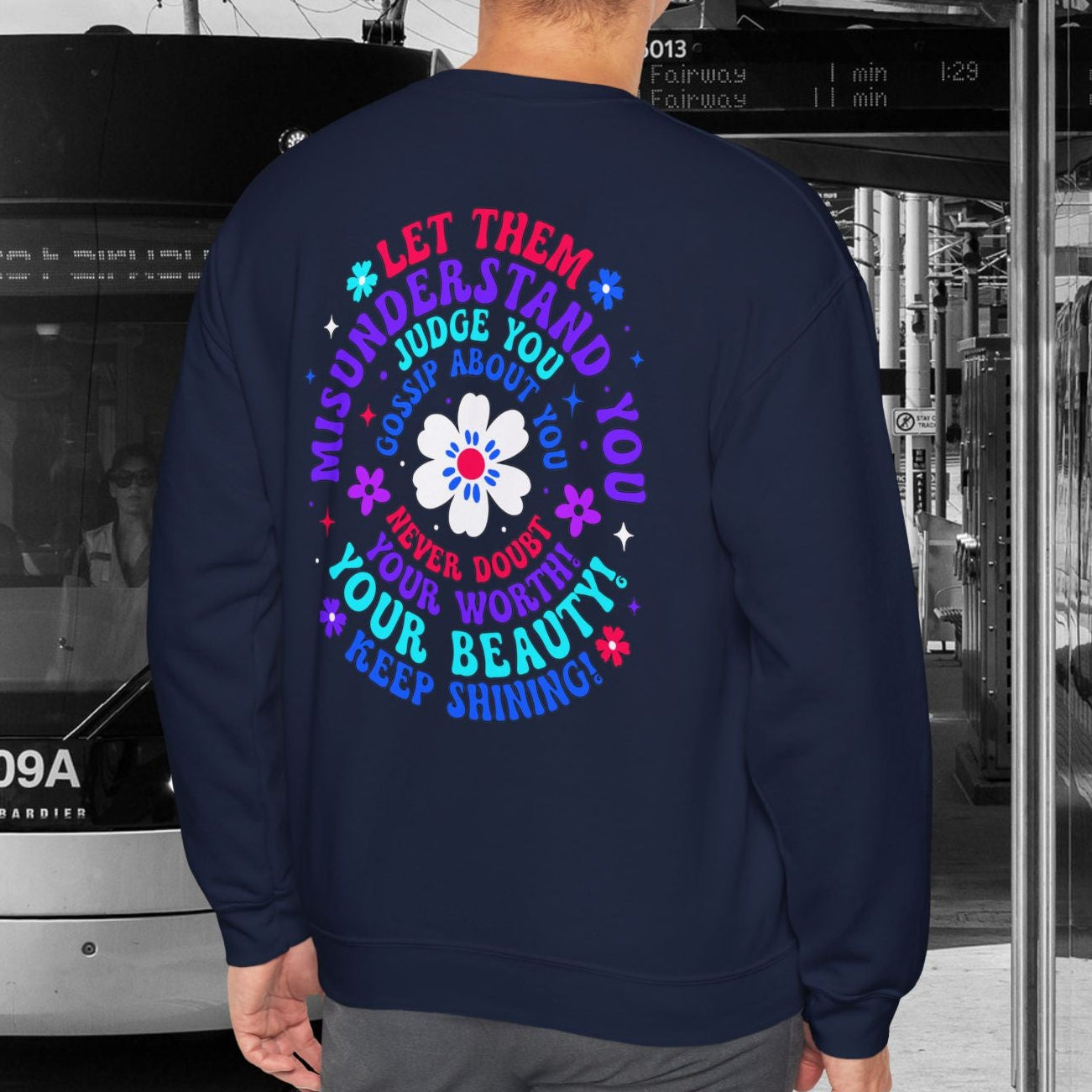 Person wearing a navy sweatshirt with colorful text and design, standing in front of a tram.