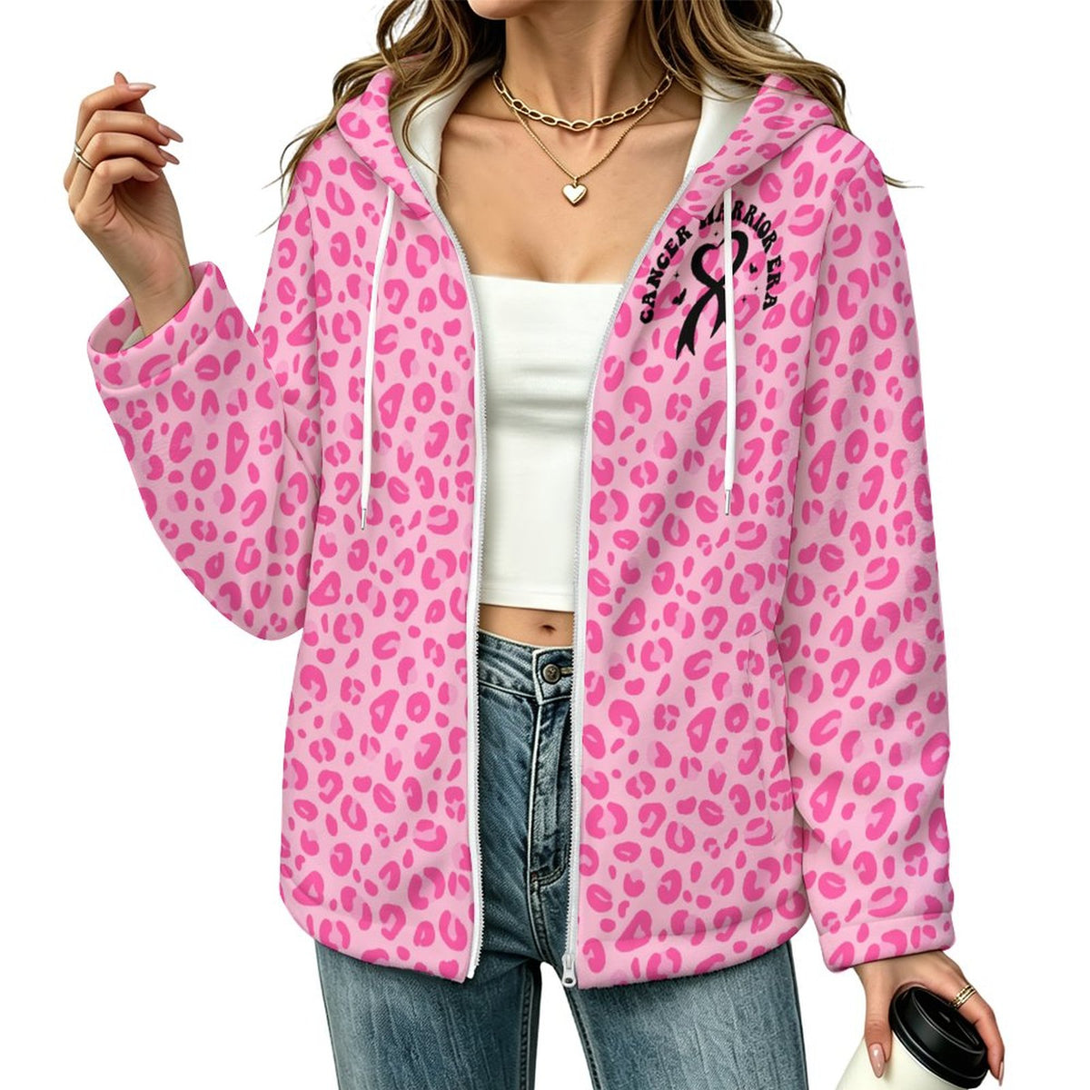 A woman wearing a pink leopard-print zip-up hoodie with white drawstrings and a black 'CANCER WARRIOR ERA' ribbon graphic on the left chest. She is also wearing a white crop top and blue jeans against a plain white background.