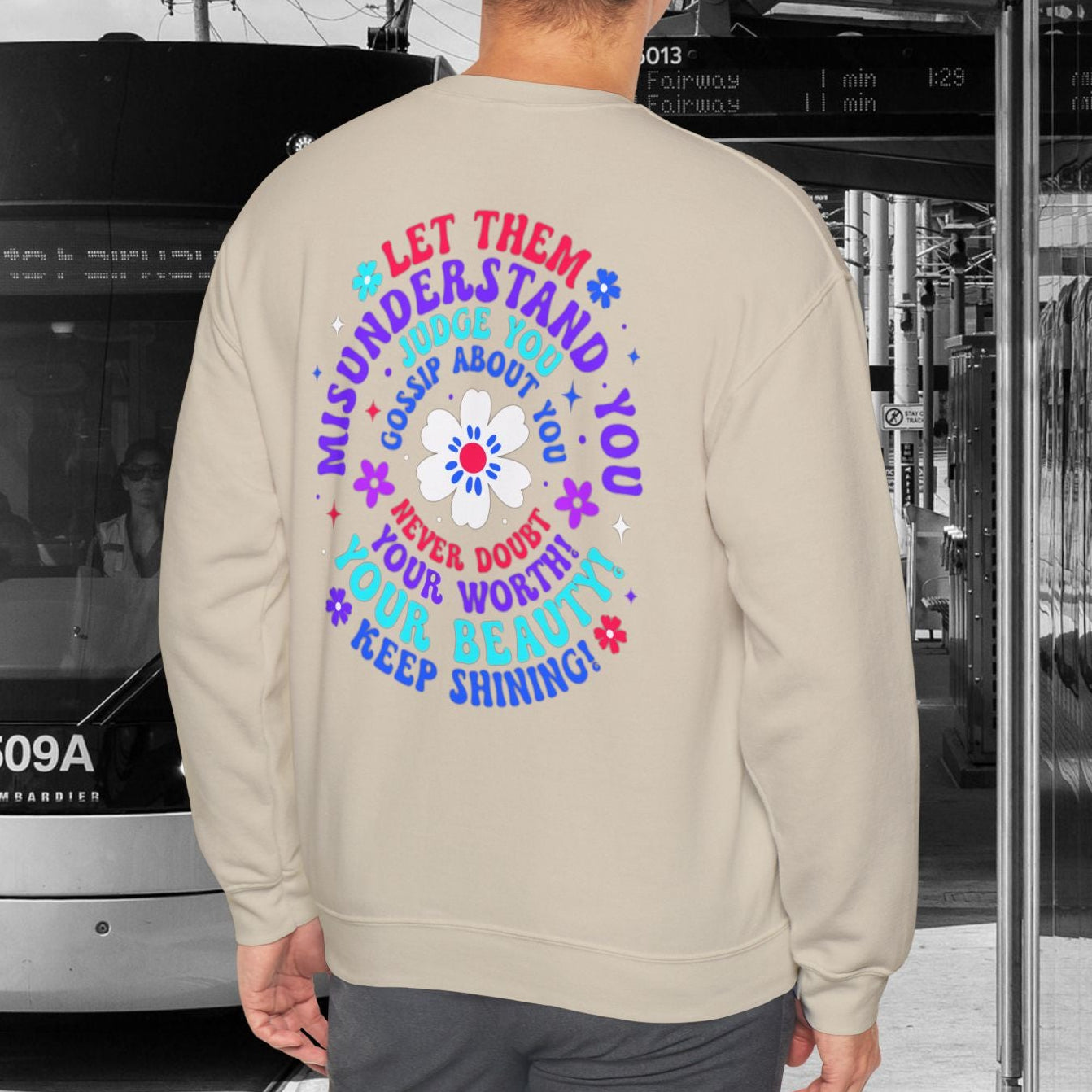 Person wearing a sweatshirt with colorful text design standing in front of a tram.