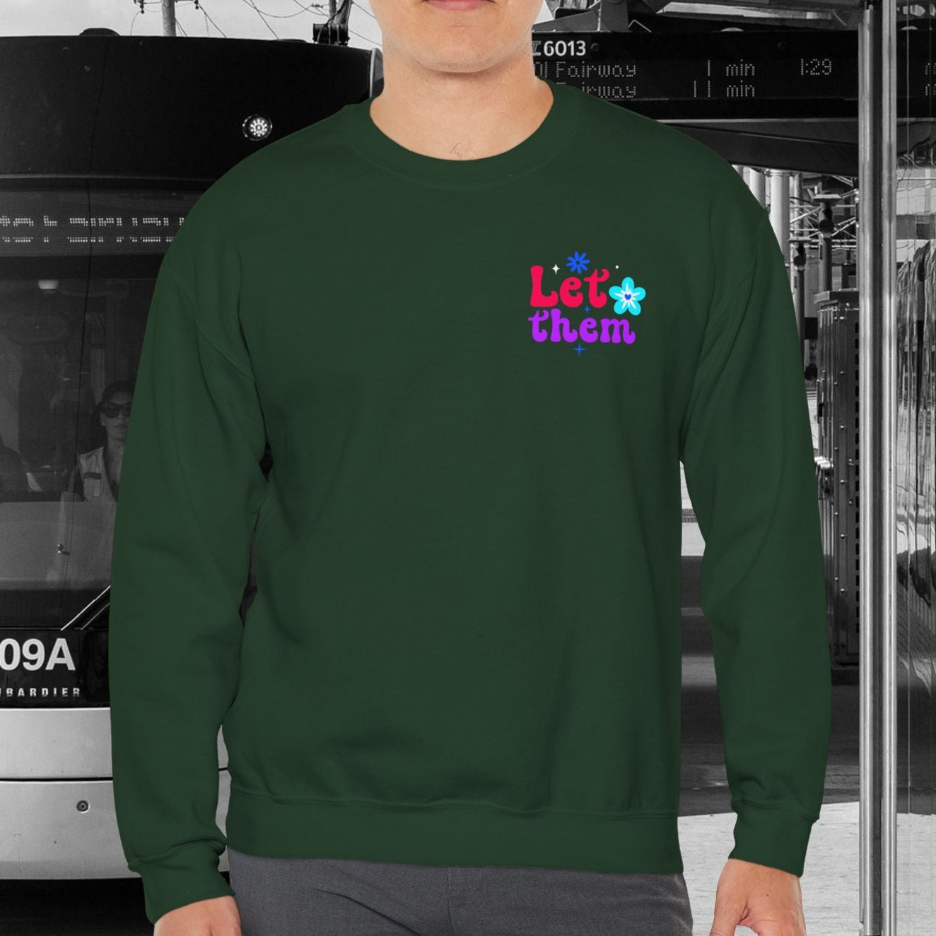Person wearing a green sweatshirt with colorful text in an urban setting with a tram.