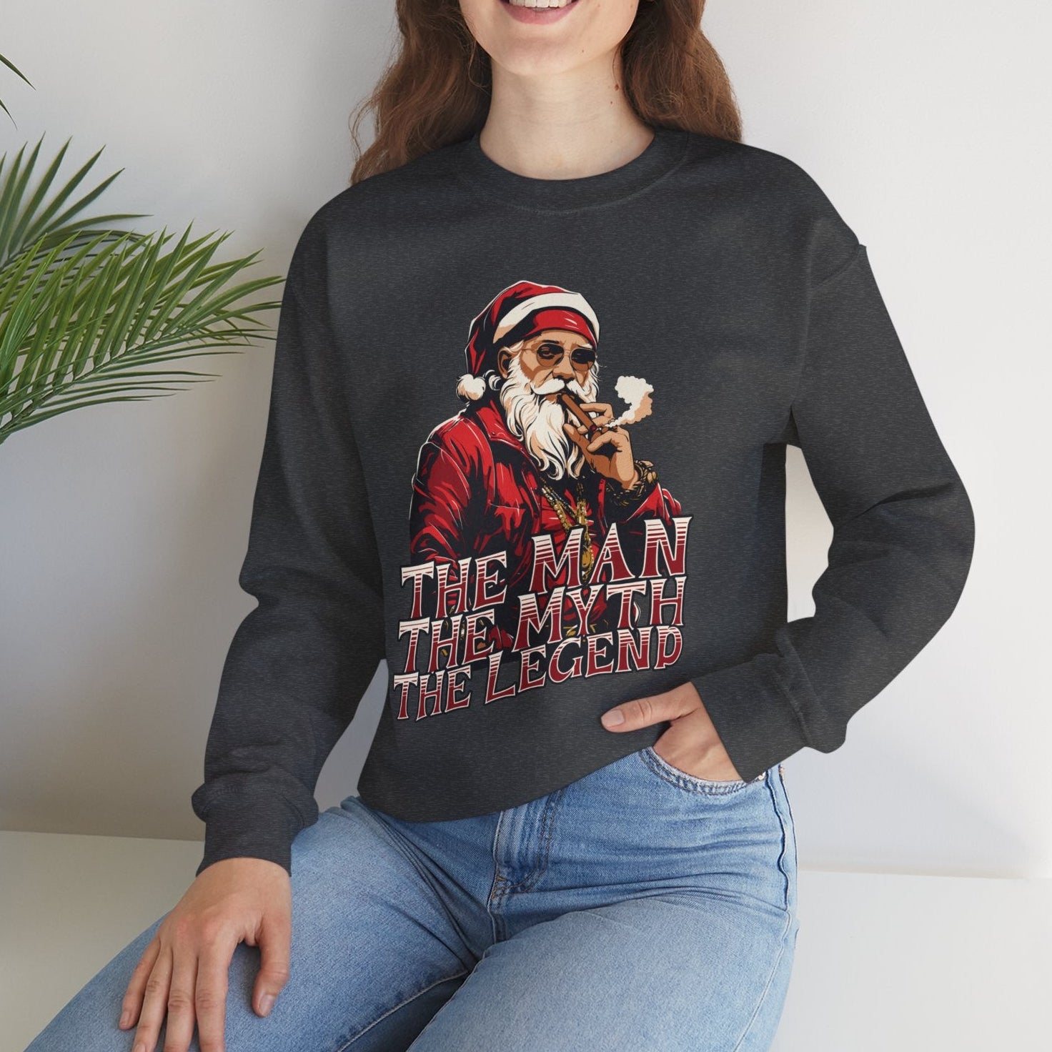 Person wearing a charcoal sweatshirt with a graphic design and text, sitting on a white surface with a plant in the background.