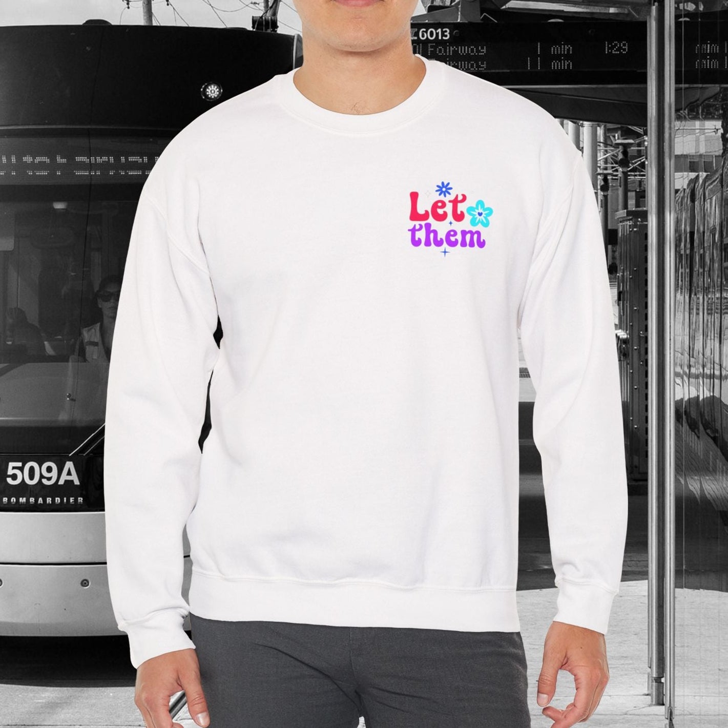 Person wearing a white sweatshirt with colorful text standing in front of a tram.