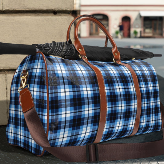 Blue plaid duffel bag with brown leather straps on a metal surface outdoors.