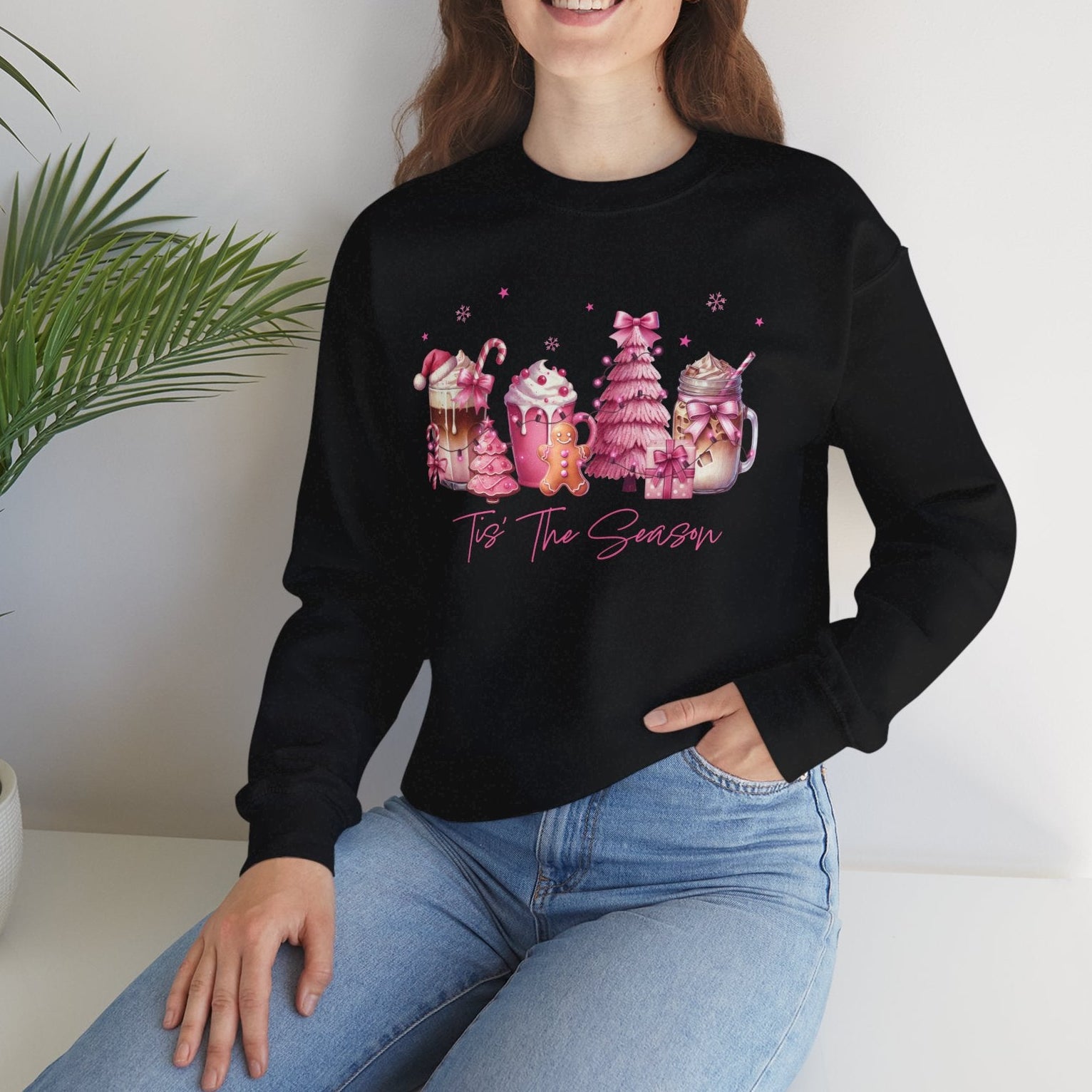 Person wearing a black sweatshirt with colorful designs and text, sitting on a white surface with a plant in the background.