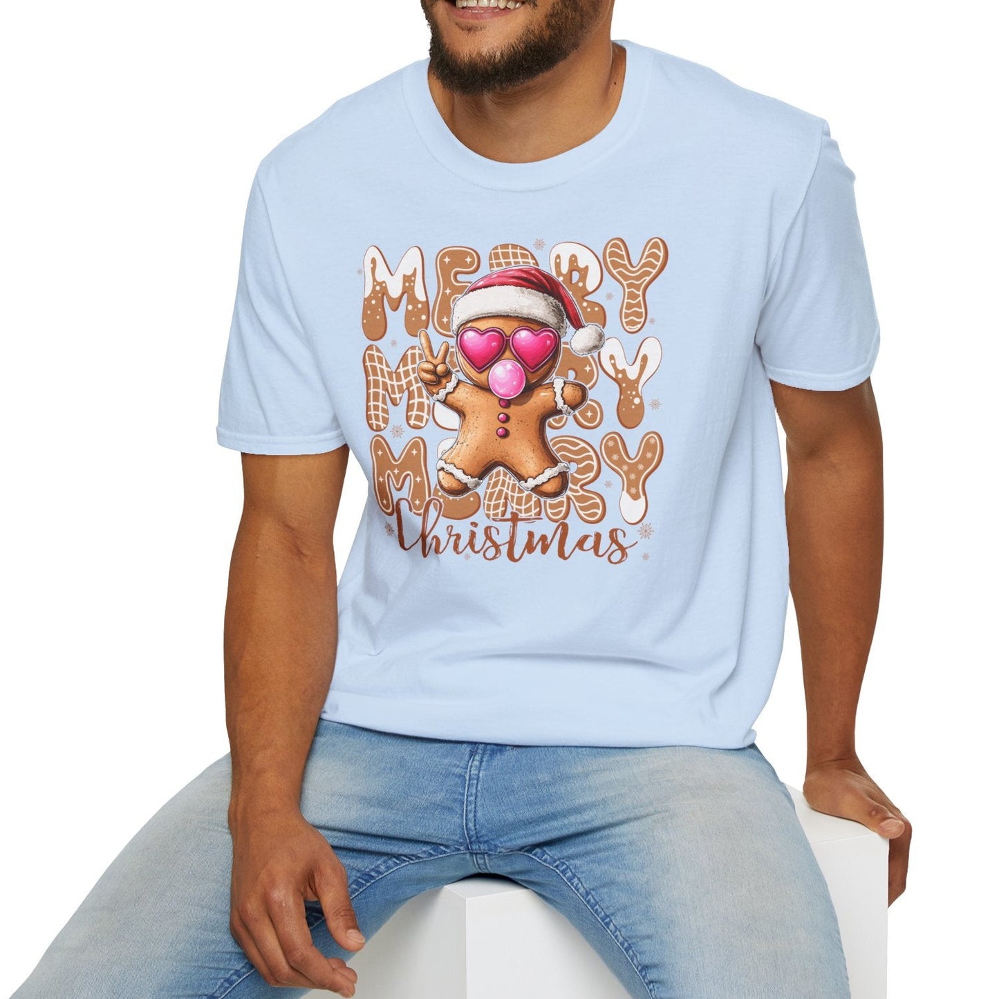 Man wearing a light blue t-shirt with a Christmas-themed design, sitting on a white stool against a white background.
