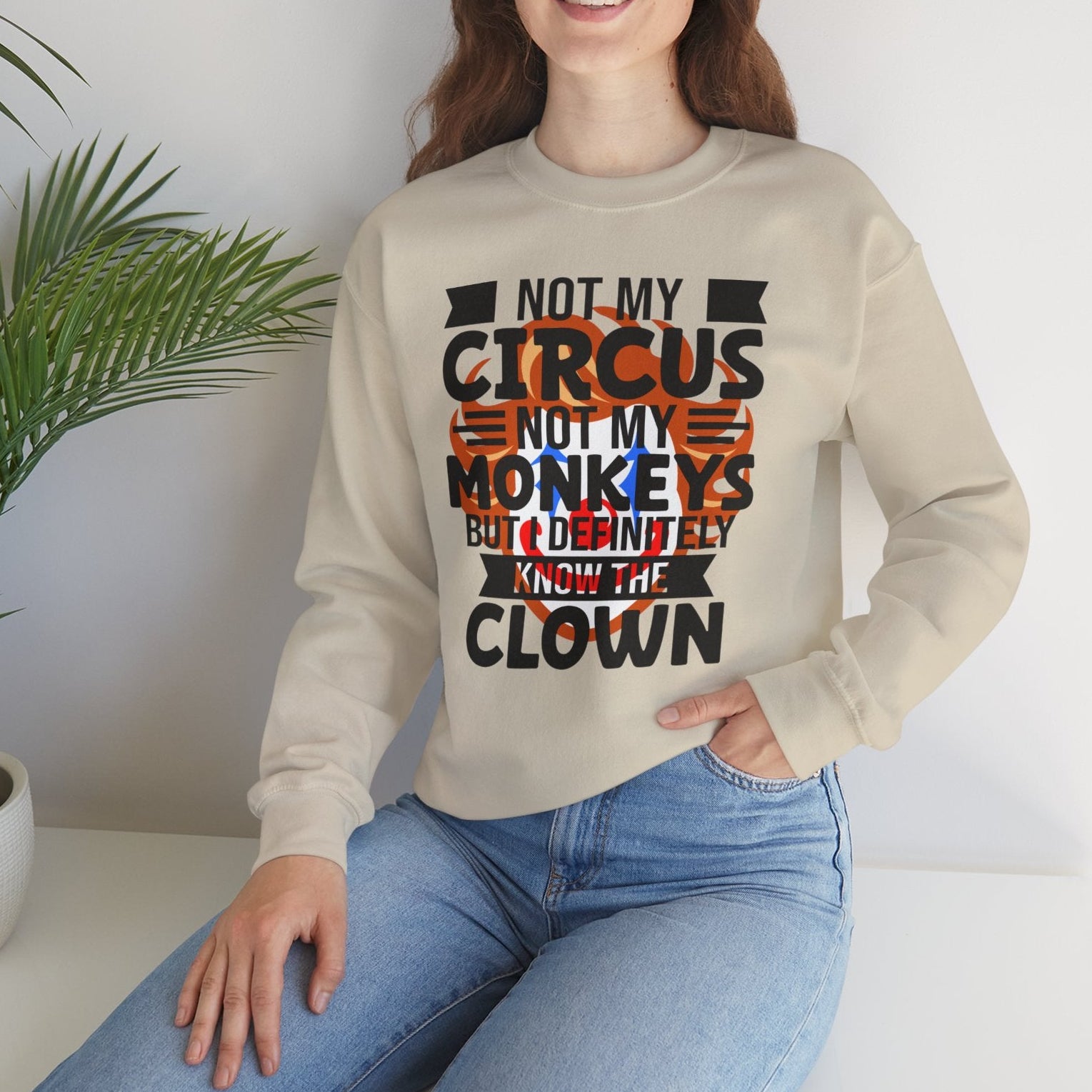 Woman wearing a beige sweatshirt with text, sitting on a white surface with a plant in the background.